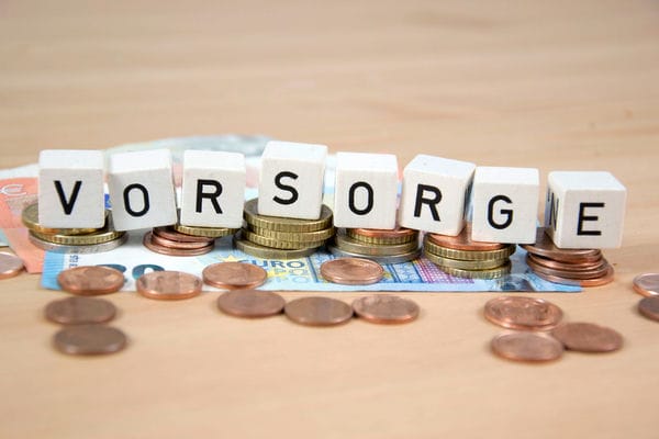 Kleine Würfel mit Buchstaben, welche Altersvorsorge bilden, liegen auf einen Haufen Geld.