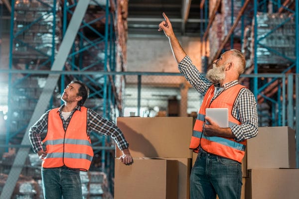 berufsinformation-karrierre-in-der-logistik Zwei Mitarbeiter besprechen ihre Aufgaben in einem großen Lager.
