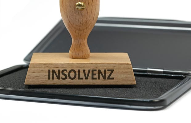 insolvenz Ein hölzerner Stempel mit dem Aufdruck „INSOLVENZ“ steht auf einem schwarzen Stempelkissen vor weißem Hintergrund.