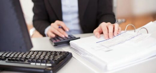 Ein Steuerberater arbeitet an einem Schreibtisch mit einem Taschenrechner, einem Computer-Keyboard und einem geöffneten Ordner mit Dokumenten.