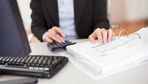 Ein Steuerberater arbeitet an einem Schreibtisch mit einem Taschenrechner, einem Computer-Keyboard und einem geöffneten Ordner mit Dokumenten.