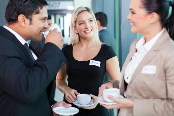 kompetenzen-networking Drei Geschäftsleute mit Namensschildern unterhalten sich lächelnd bei einer Tasse Kaffee während eines Networking Event.