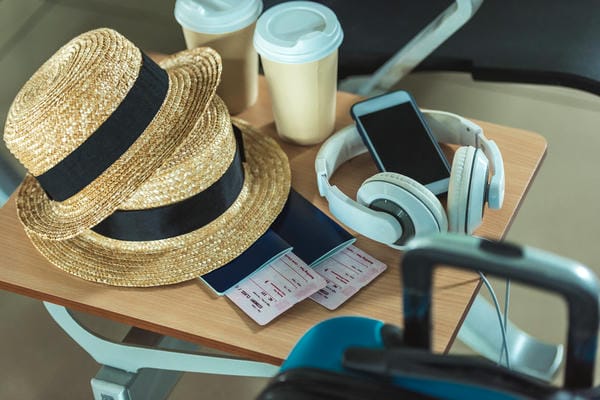 urlaub-betriebsferien Reiseutensilien wie Strohhüte, Pässe und Kaffeebecher liegen für den Urlaubsantritt während der Betriebsferien auf einem Tisch bereit.