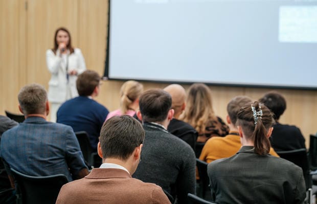 weiterbildung-offenes-seminar Eine Rednerin hält ein offenes Seminar vor einem sitzenden Publikum in einem modernen Konferenzraum.